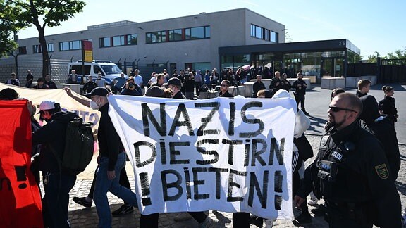 Demonstranten aus dem linken Spektrum laufen vor Beginn der Urteilsverkündung gegen Lina E. und drei Männer vor dem Oberlandesgericht (OLG) Dresden mit einem Banner „Nazis die Stirn bieten“ entlang.