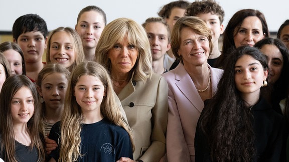 Brigitte Macron (Mitte l), Ehefrau des Präsidenten von Frankreich, und Elke Büdenbender (Mitte r), Ehefrau des Bundespräsidenten, stehen im Romain-Rolland-Gymnasium zwischen Schülerinnen und Schülern. 