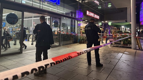 Polizeibeamte stehen vor einem Supermarkt, dessen Eingang nach einem blutigen Streit abgesperrt wurde.