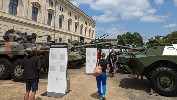 Besucher eines Militärmuseums laufen zwischen Panzern unterschiedlichen Typs entlang. 