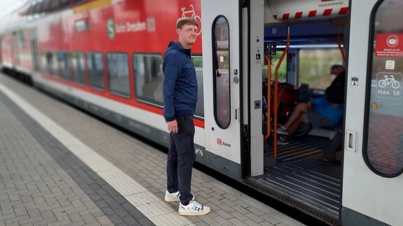 Ein Mann in dunklem T-Shirt und Hose steht an einer Tür einer geöffneten S-Bahntür auf dem Bahnsteig und ist im Begriff, einzusteigen. 