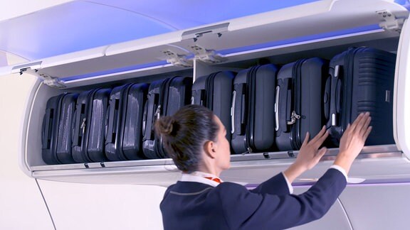 Eine Stewardess räumt Koffer in Gepäckfächer.