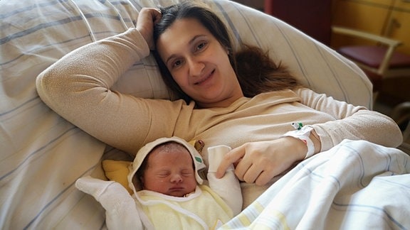 Mutter Cindy Ihle liegt in einem kKlinikbett und hält ihre neugeborene Tochter Tiana Jasmin - das Neujahrsbaby 2024 im Uniklinikum Dresden - im rechten Arm. 
