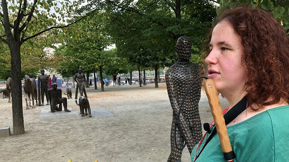 Die blinde Kunstvermittlerin Lydia Hänsel steht vor Bronze-Skulpturen des tschechischen Künstlers Michal Gabriel. Die Figuren zeigen u.a. Pferde, Raubkatzen und Menschen mit überlangen Armen. 