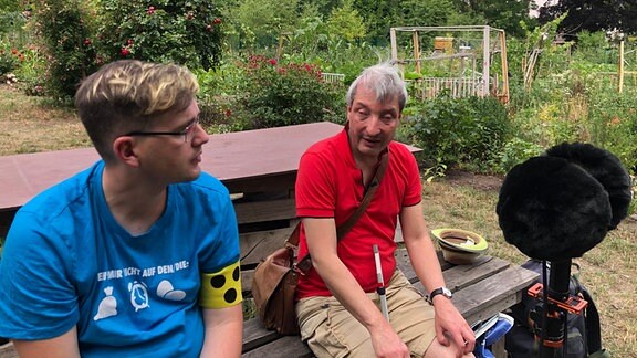 Marco Rademann und Daniel Martin sitzen gemeinsam auf einer Bank im internationalen Garten.