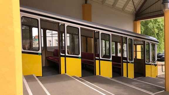 Der gelbe Wagen der Standseilbahn steht in der Bergstation und hat die Türen geöffnet.