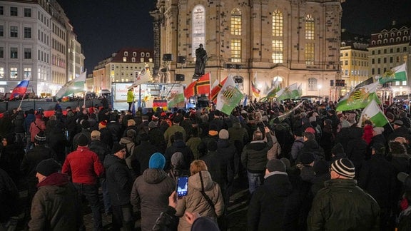 Pegida-Anhänger stehen in Dresden vor der Frauenkirche. Es wehen Fahnen der Freien Sachsen, von Russland und deutsche Fantasiefahnen.