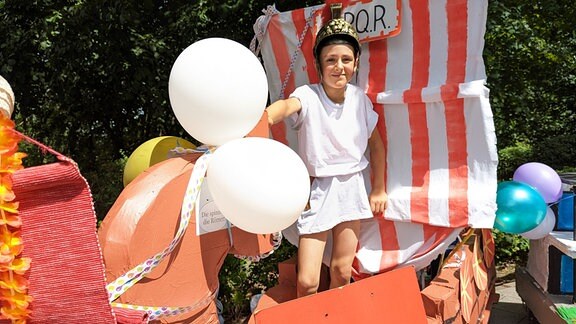 Eine Junge ist als Legionär verkleidet und steht in einem Seifenkisten-Boot. 