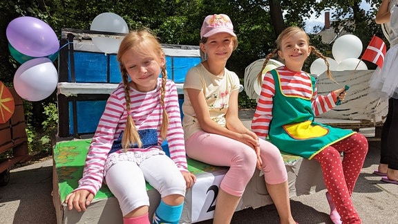 Drei Mädchen sind als Pippi Landstrumpf verkleidet und sitzen auf einer Villa-Kunterbunt-Seifenkiste. 
