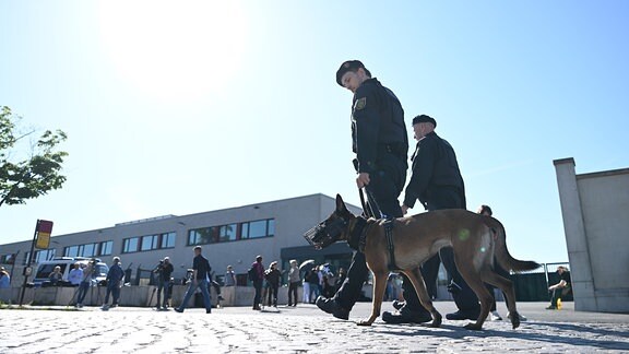 Polizisten mit einem Spürhund laufen vor dem Oberlandesgericht Dresden entlang