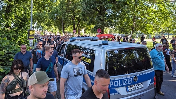 Menschenmenge auf einer Straße, dazwischen Polizeiauto