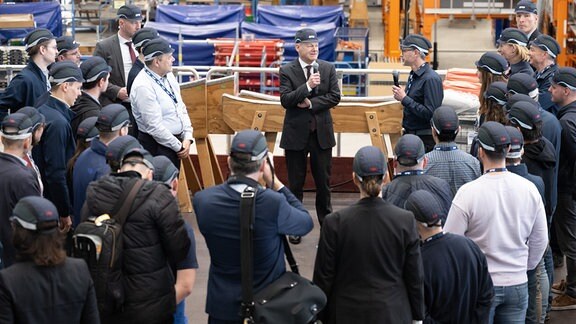 Bundeskanzler Olaf Scholz (SPD, M) spricht bei seinem Besuch der Elbe Flugzeugwerke in einem Hangar mit den Mitarbeitern der Flugzeugwerke. 
