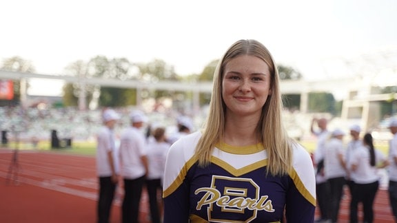 Eine junge Frau im Cheerleader-Outfit schaut freundlich in die Kamera.