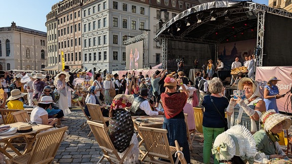 Auf dem Neumarkt Dresden stehen verkleidete Menschen vor einer Bühne und warten auf das Ergebnis der Stadtwette.