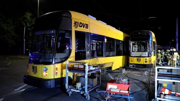 Zwei Straßenbahnen stehen auf einer Straße, es ist nacht.