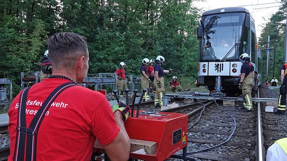 Feuerwehrleute heben mit hydraulischer Technik eine Straßenbahn zurück auf Gleis