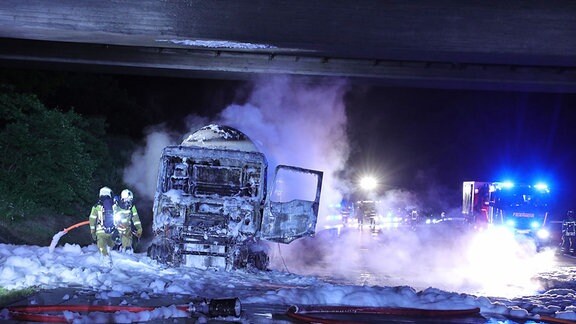 Feuerwehrleute löschen mit viel Schaum einen brennenden Gefahrguttransport.