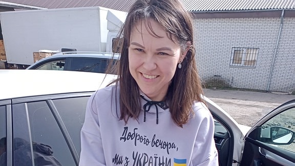 Frau mit dunklen Haaren und pinkem Pullover mit ukrainischer Flagge lächelt in Kamera