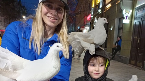 Blonde Frau mit Basecap und einem kleinen Jungen lässt weiße Tauben aufsteigen