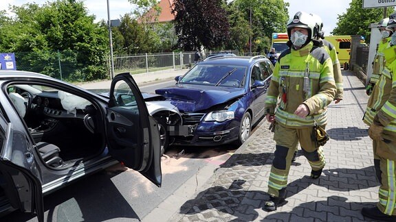 Ein blaues Auto ist auf der falschen Straßenseite frontal in ein silbernes Auto gefahren. Die Fahrer- und Beifahrertüren stehen offen. Feuerwehrleute laufen umher und versuchen ausgelaufenen Treibstoff zu binden und zu beseitigen. De Unfall passierte am 24.05.2020, mittags gegen 12:30 Uhr in Dresden-Gohlis.