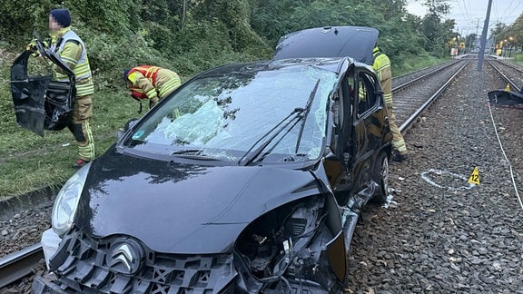 Rettungskräfte sichern ein mit einer Straßenbahn kollidiertes Auto ab.