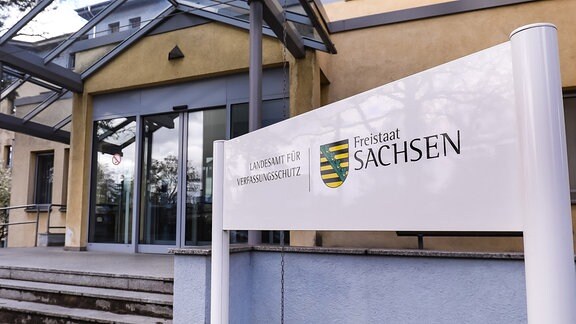 Eingang eines Gebäudes, davor ein Schild mit der Aufschrift Landesamt für Verfassungsschutz Sachsen