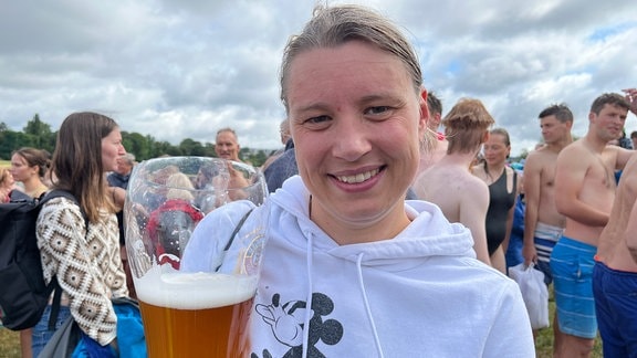 Eine junge Frau mit weißem Pullover hält ein Bierglas in der Hand. 