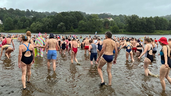 Zahlreiche Menschen laufen zum Schwimmen in einen Fluss.