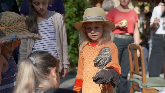 Ein Mädchen mit Strohhut im Publikum hält eine Eule