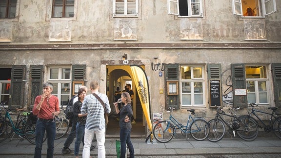 Menschen vor einem baufälligen Gebäude mit Fahrrädern an der Hauswand