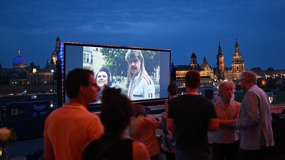 Zahlreiche Gäste der "Filmnächte am Elbufer" sitzen und stehen vor der Kulisse der Dresdner Altstadt und schauen auf eine Kinoleinwand.