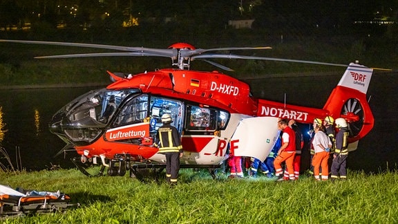 Ein Rettungshubschrauber steht nachts am Elbufer, Sanitäter bringen eine verletzte Frau.