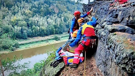 Zwei Retter kümmern sich auf einem Felsvorsprung um einen verunglückten Wanderer