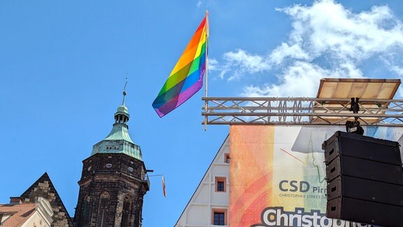 Regenbogenfahnen an einer Bühne und an einem Kirchturm