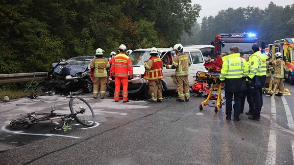 Verkehrsunfall mit drei zerstörten Autos auf der nassen und abschüssigen Straße, Rettungsdienst und Feuerwehr.