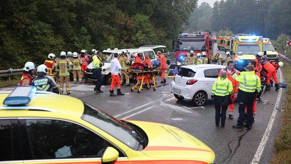 Verkehrsunfall mit drei zerstörten Autos auf der nassen und abschüssigen Straße, Rettungsdienst und Feuerwehr.