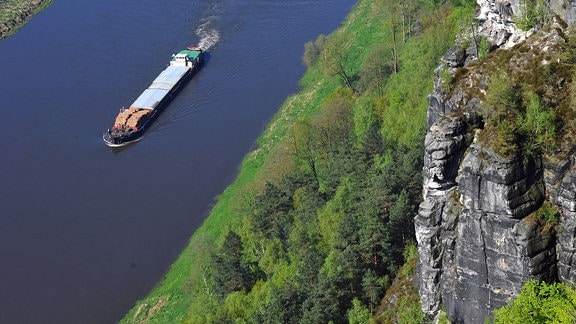 Ein Güterschiff fährt in Rathen (Sachsen) im Nationalpark Sächsische Schweiz auf der Elbe an den Sandsteinfelsen des Basteimassivs vorbei. 