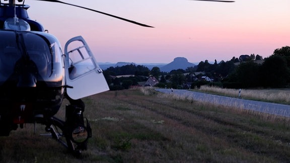 Eine Hubschrauber steht in den Abendstunden auf einem Feld. 