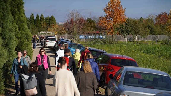 Menschen laufen neben geparkten Autos