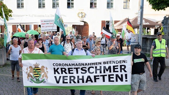 Teilnehmer einer Kundgebung der rechtsextremen Kleinstpartei Freie Sachsen gehen anlässlich einer CDU-Wahlkampfveranstaltung über den Marktplatz von Pirna und tragen ein Transparent mit der Aufschrift "Kretschmer verhaften".