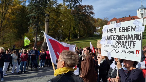 Rund 100 Menschen stehen vor einer Klinik in der Mittagspause und protestieren gegen schlechte Arbeitsbedingungenund das agieren ihrer Klinikleitung.