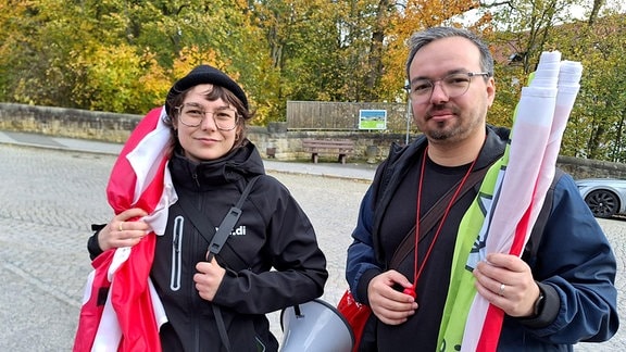 Zwei Gewerkschaftssekretäre von Verdi stehen mit zusammengerollten Verdifahnen und einem Megafon vor einer Klinik und protestiert gegen schlechte Arbeitsbedingungen und das Agieren der Klinikleitung.