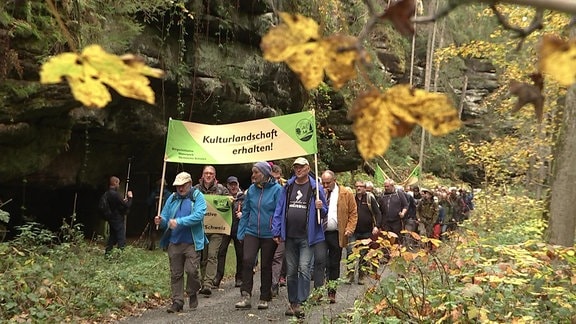 Eine Gruppe von Menschen wandert mit Bannern durch den Wald, um sich für die Öffnung von historischen, grenzüberschreitenden Wanderwege einzusetzen.