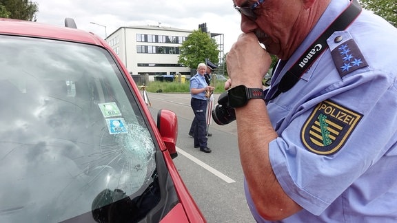 Ein Polizist blickt auf die Frontscheibe des Autos, wo der Aufprall erfolgt ist.