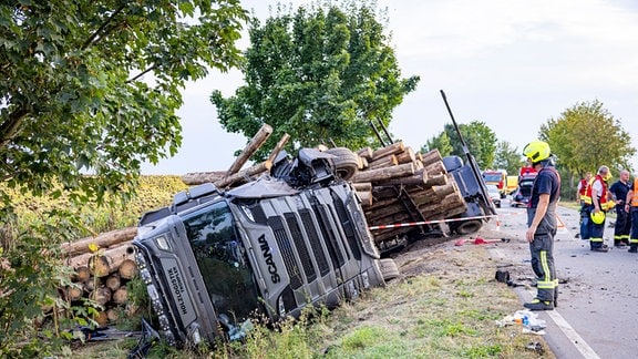 Ein Feuerwehrmann steht an einem umgestürzten Holzlaster.