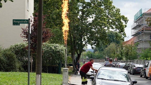 In einem Wohngebiet ist am Straßenrand eine in die Höhe schießende Flamme zu sehen.