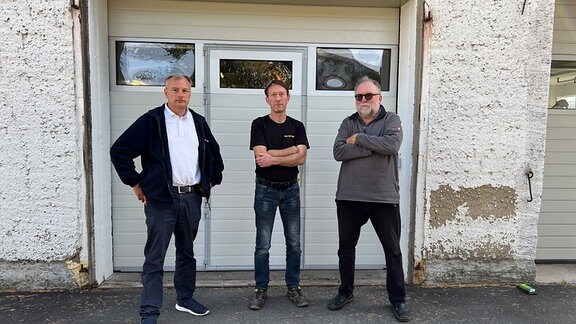Drei Männer stehen vor einem Werkstattgebäude.