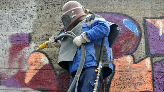 Ein Arbeiter mit Schutzhelm entfernt ein Graffiti. 