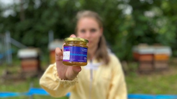Eine junge Frau zeigt ein Glas Honig.