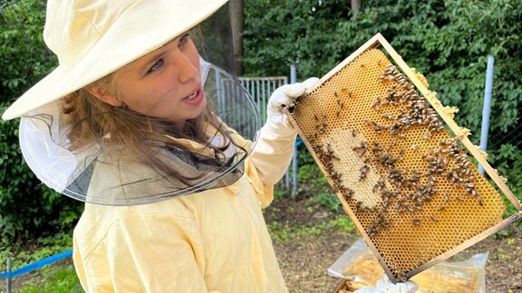 Eine junge Frau hält eine Bienenwabe in der Hand